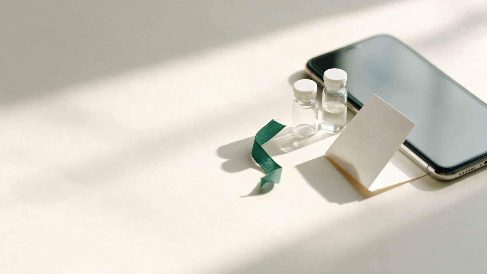 A phone lying face down next to two small glass vials and a blank card.